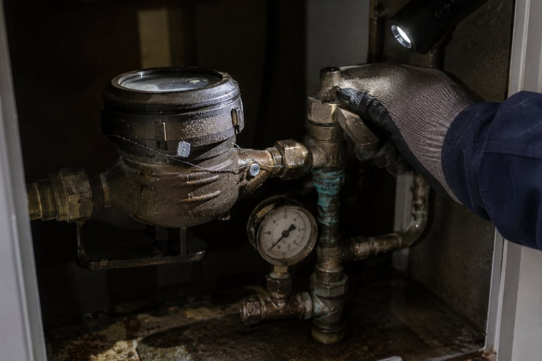 Revisión de un contador de agua y su manómetro con linterna dentro del armario